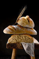 Composition from crusty sourdough baguette, bread loaf and bun on a rustic wooden stool with ear...