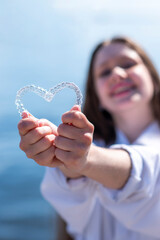Dental care. Smiling beautiful girl holding heart-shaped aligners. Plastic retainers for teeth alignment.