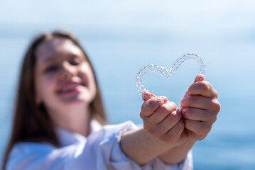 Dental care. Smiling beautiful woman holding heart-shaped aligners. Plastic retainers for teeth alignment.