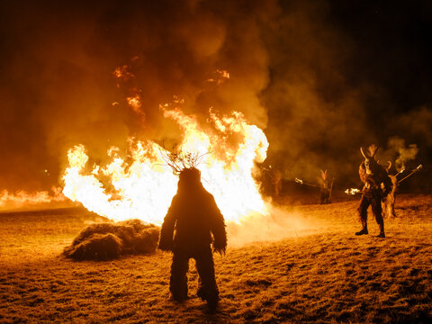 Silhouetted figures in traditional Krampus costumes stand before a large bonfire at night. Krampus and St Nicholas, 5 December in Tarvisio, Friuli Venezia Giulia, Julian Alps, Italy.