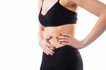 Close-up of a woman holding her stomach, dressed in black activewear, with a white background, representing concepts such as fitness, health, or abdominal discomfort.