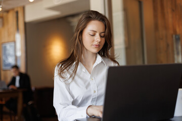 Elegant young woman working remotely on her laptop in a bright, modern cafe. Perfect representation...