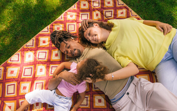 Happy family relaxing together on blanket in park - Powered by Adobe