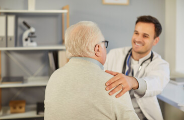 Fototapeta premium Senior sick man sitting in office during exam with young cheerful male physician. Doctor supporting his elderly patient sitting in medical clinic. Medicine and health care concept.