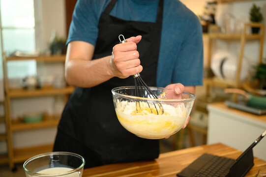 Man whisking pancake batter in a glass bowl while following recipe on digital tablet - Powered by Adobe