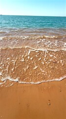 Pristine red sand beach with turquoise water gently washing coastline under bright sunlight, revealing serene tropical landscape and tranquil ocean scenery