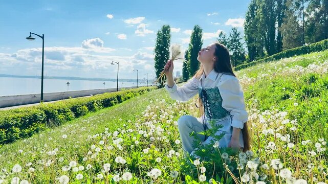 Young woman picking and blowing dandelions on a sunny day in spring