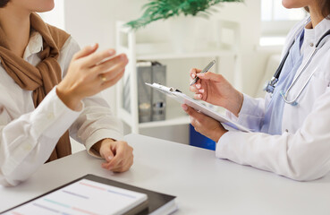 Cropped view of female doctor attentively listening to woman patient and taking notes during...