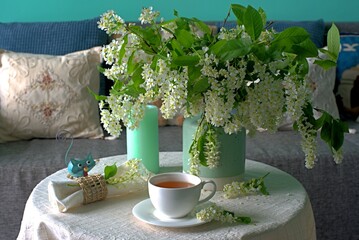 Cup of tea on the table with spring fresh bouquet with white blooming fragrant branches of bird...