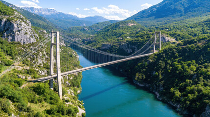 Obraz premium Stunning aerial view of massive suspension bridge spanning river, surrounded by lush green mountains and clear blue skies