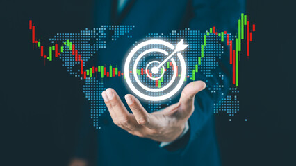 A businessman holds a digital target icon with a world map and stock chart, symbolizing global business strategy and financial goals.