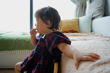 Little girl enjoying a quiet moment while sitting on a cozy bed in a bright room on a sunny day