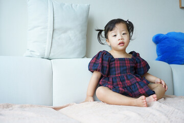 Fototapeta premium Young girl sitting on a couch wearing a plaid dress in a cozy indoor setting during daylight