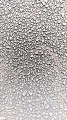 Close-up of water droplets on a smooth surface, creating a natural abstract texture. Condensation pattern with detailed droplets and light reflections.