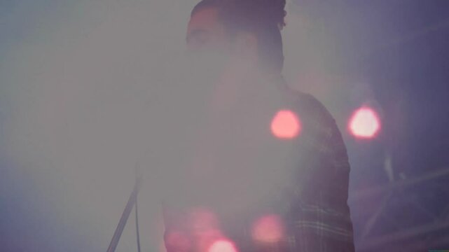Male singer gripping vintage microphone singing on hazy concert stage, with animated light flares