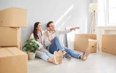 Portrait of a young happy couple man and woman sitting on floor in empty new apartment among...