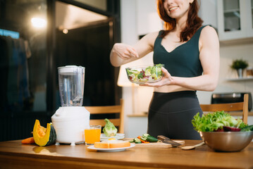Smiling woman in a modern kitchen with fresh fruits, veggies, blender, and juice, embracing clean...