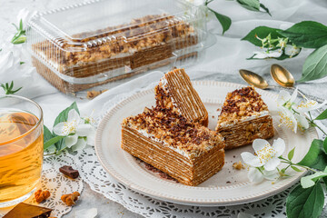 Homemade honey cake with sour cream and nuts on light background with cup of tea and spring flowers. Sweets, dessert and pastry, top view