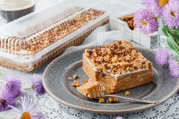 Homemade honey cake with sour cream and nuts on light background with cup of coffee and flowers. Sweets, dessert and pastry, top view, close up
