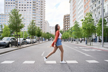 Fototapeta premium Young latin woman with braids crossing the street in the city
