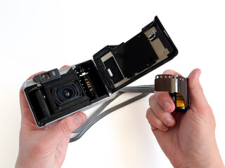 Hands loading a roll of 35mm film into an open analog camera. Photography concept. Analog photo shooting. Inserting film into a vintage camera. Old-fashioned photography process.