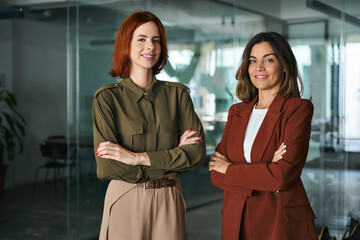 Two smiling confident ladies standing arms crossed in office. Women partnership concept, portrait....