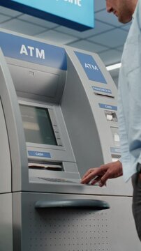 Cash Machine in Crowded Airport Terminal: Man Pressing Buttons on ATM Keypad, Entering PIN Code, Withdrawing Cash, Taking Money. Automated Teller Machine, Banking Services, Transactions. Vertical Shot