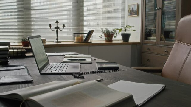 No people view of priests office featuring leather chair and large desk with open laptop, books, holy bible and rosary beads