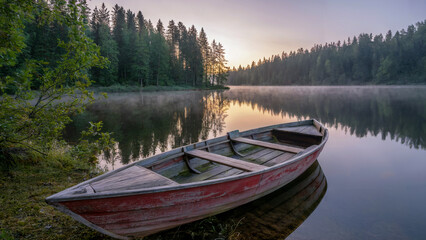 Obraz premium Wooden rowboat rests peacefully on the shore of a misty lake at sunrise reflecting nature