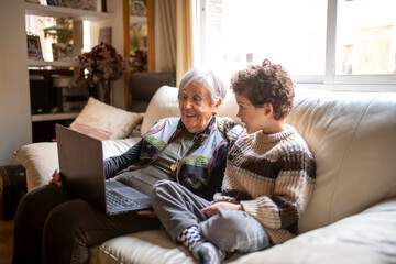 Grandmother and grandchild sharing precious moments with laptop on sofa