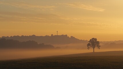 Sunrise over misty hills with silhouetted tree and distant cross in tranquil landscape