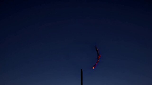 Fiery ring of flames spins against dark sky, glowing with vibrant orange and red hues in a smooth, mesmerizing looping video animation