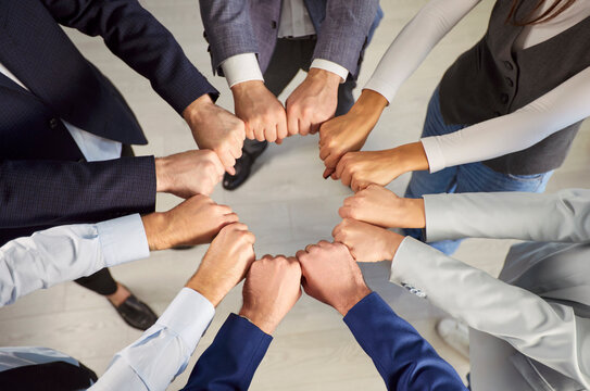Top-down shot of business people standing in a circle and holding fists together, working together in the office. Emphasizing teamwork, collaboration, and unity within the work team. - Powered by Adobe