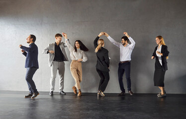 Happy overjoyed young diverse employees group dance, workers relaxing dancing company colleagues celebrate shared business success or victory joy winners in office near grey wall background 
