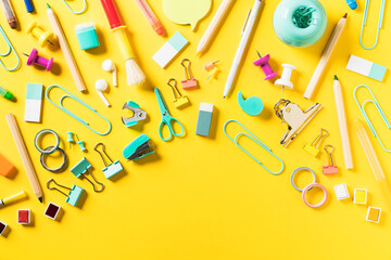 Colorful school and office supplies scattered on yellow background