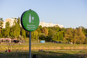 Green public sign indicating Alcohol consumption allowed with bottle and glass icon in outdoor park area regulating activity