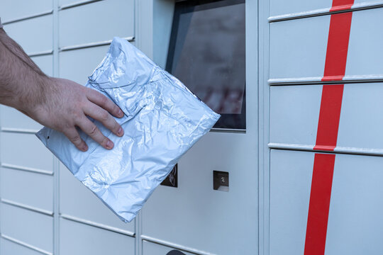 Customer hand depositing package into open compartment of automated parcel locker illustrating modern e-commerce self-service shipping