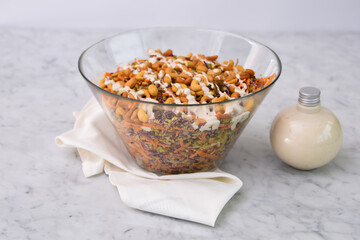 Fresh Broccoli Salad with Cashews in a clear glass bowl on napkin with broccoli florets, crunchy cashews, shredded carrots, and red cabbage, drizzled with creamy white sauce bottle side view
