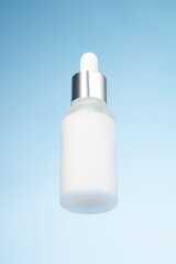 White unbranded dropper bottle on glass against blue background. Skin care product presentation. Trendy showcase . bottom view