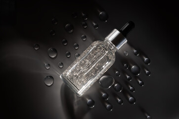 Glass bottle facial essential oil or serum packaging on gray matte background with plenty of transparent water drops. Beauty cosmetic product for skincare concept. minimal and luxury style.