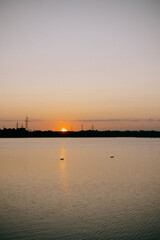 Obraz premium Peaceful sunset over calm river with clear sky and electric towers on horizon perfect for serene nature backgrounds, evening reflections and tranquil outdoor visuals