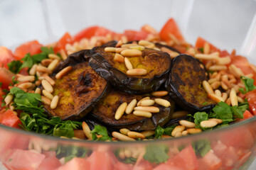 Mediterranean Couscous Salad with Grilled Eggplant featuring fluffy couscous, tomatoes, parsley, grilled eggplant slices, and toasted pine nuts with bottle of olive oil closeup view of healthy salad