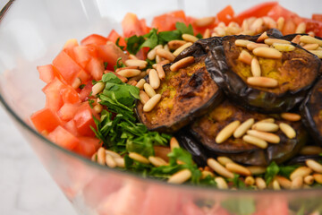 Fresh Mediterranean Couscous Salad with Grilled Eggplant featuring couscous, tomatoes, parsley, grilled eggplant slices, and toasted pine nuts with bottle of olive oil closeup side view