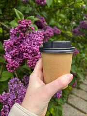 paper coffee cup on a background of purple lilacs