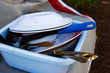 A blue plastic basin full of used dishes, pans, and utensils after a meal at a forest campsite in...