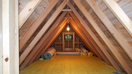 Construction of Attic with Exposed Beams and Yellow Insulation Under Ceiling Light