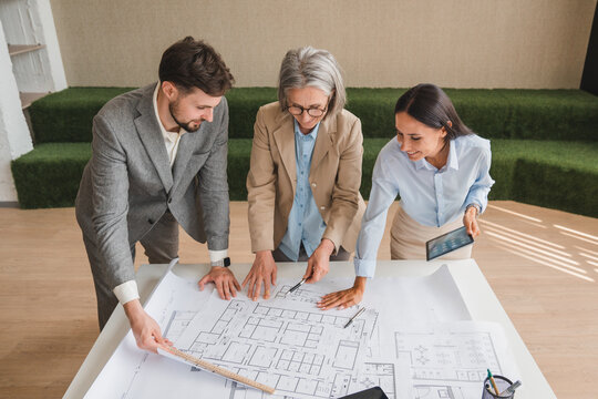 Team of multiethnic architects working on construction plans in meeting room. Engineers discussing on project in office. Businesswoman and her colleagues standing around table working on blueprint.