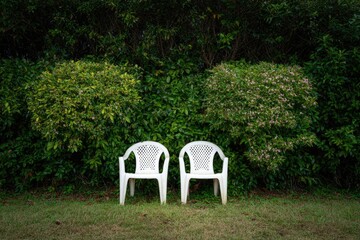 Two white plastic chairs facing each other in a garden