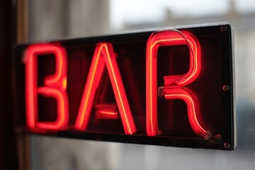 Bright red neon sign illuminates bar entrance in urban setting during evening hours