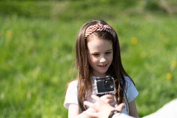 Cute smiling girl in a T-shirt stands taking pictures on a camera standing in the summer on a green...
